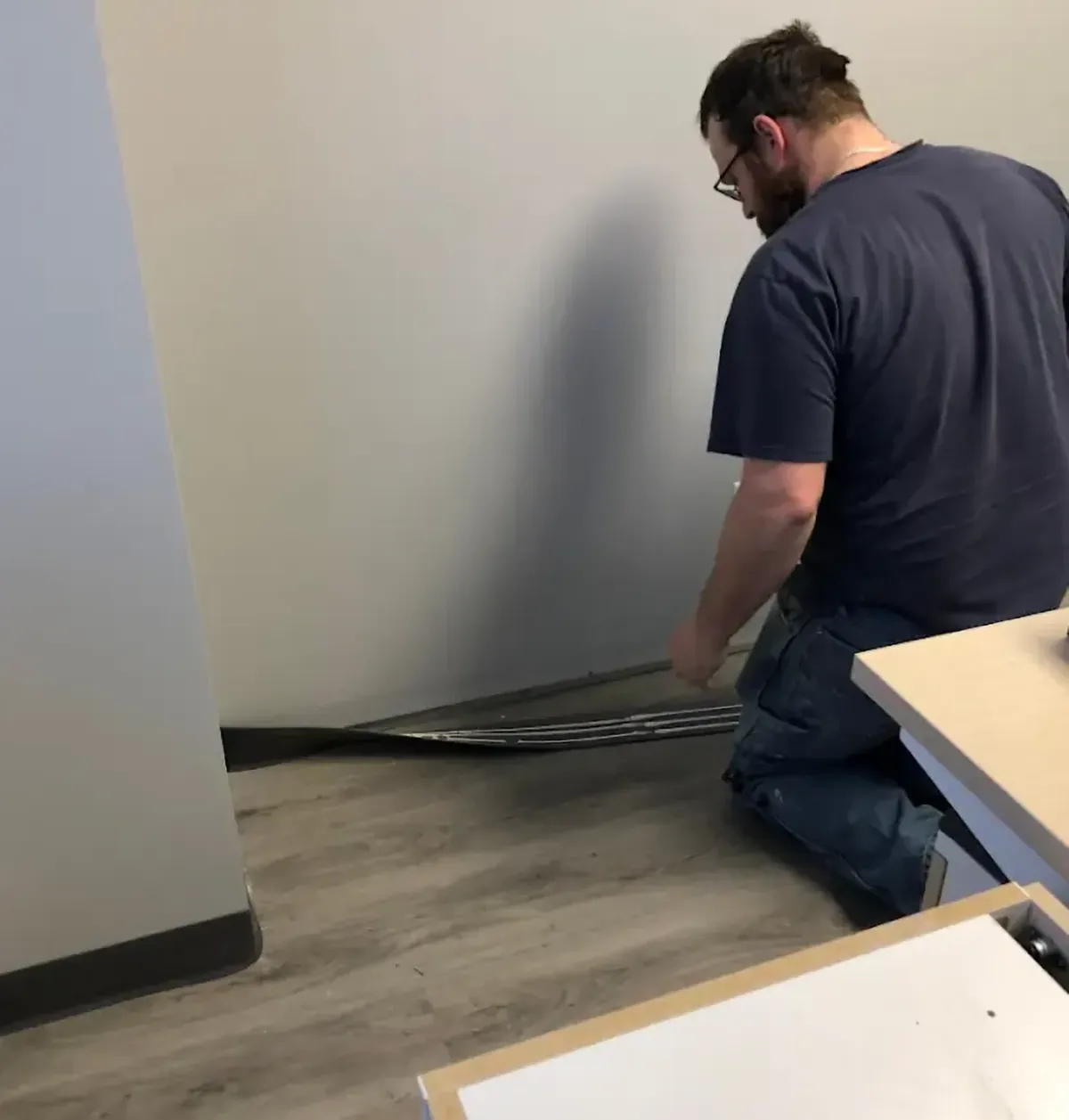 An installer fitting vinyl wall base along new plank flooring in an office